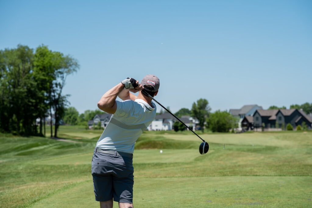 man in white t-shirt and black pants holding golf club during daytime
